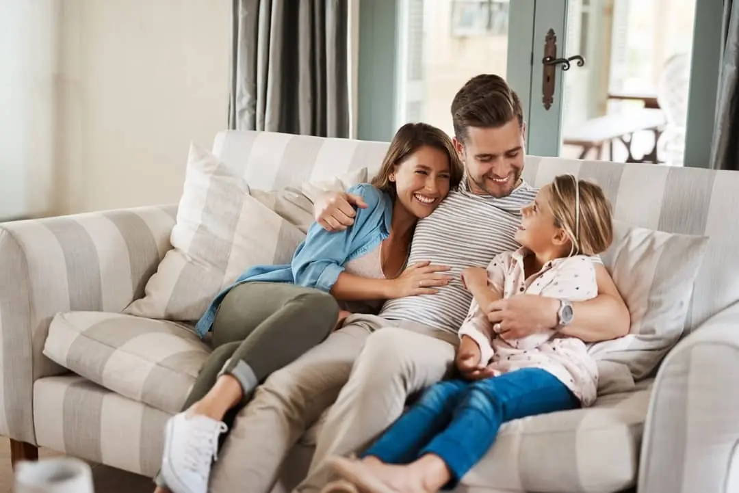 Família somrient al sofà de casa seva
